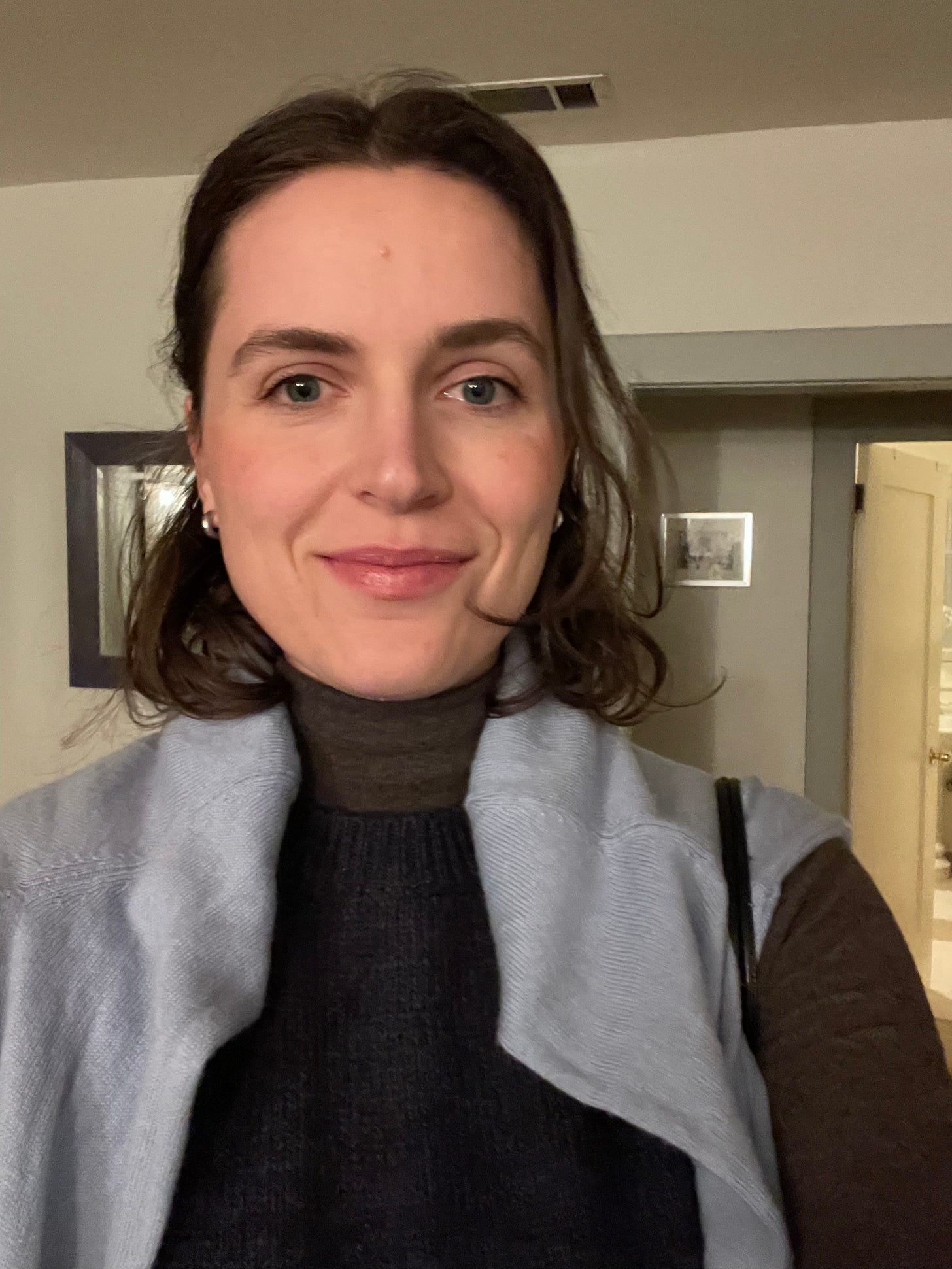 Woman smiling wearing a sweater over her shoulders with a short hair cut