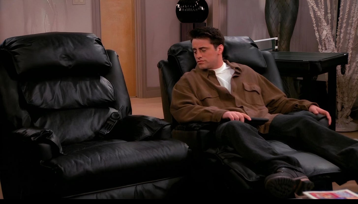 Screencap from a Friends episode; Joey is in his recliner looking at Chandler's recliner, which is empty.