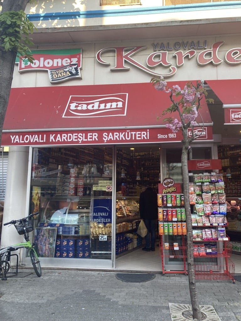 Deli on Buyukada island with red awning and display of chips and nuts outside the glass window.