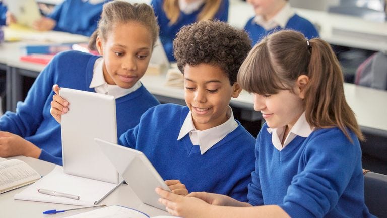 Crianças do ensino fundamental vestindo uniformes escolares azuis usando tablets digitais na mesa da sala de aula foto de stock