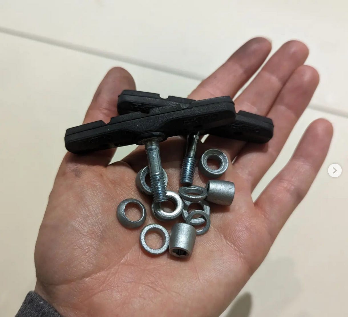 a hand is holding two brake pads and a bunch of different washers