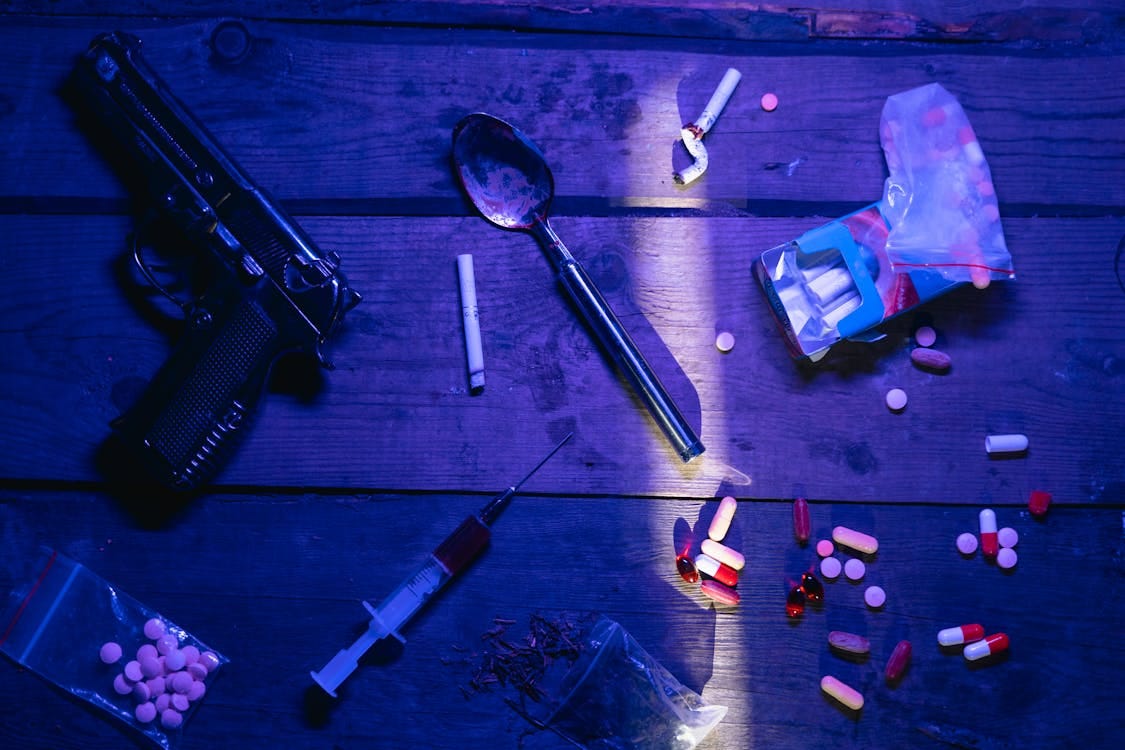 Free Intriguing still life image depicting pills, a gun, and syringe under dramatic lighting. Stock Photo