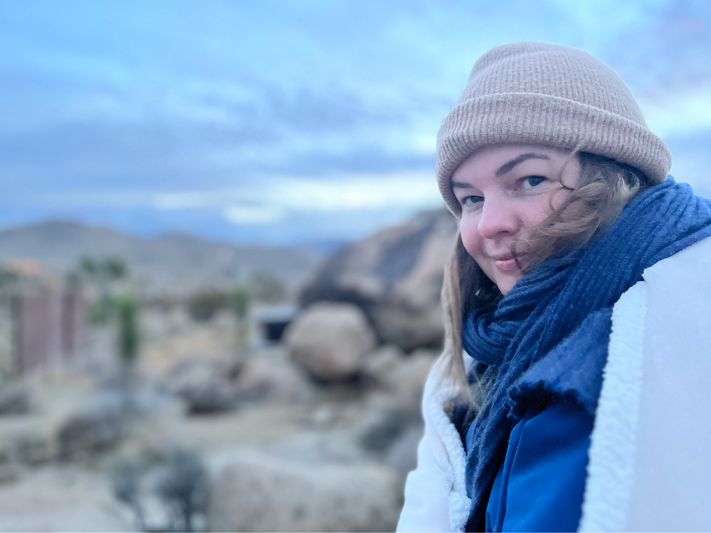 A photo of Amber looking into the camera, smiling slightly. A desert landscape is out of focus behind her.