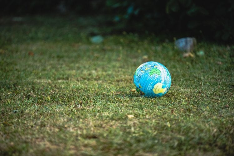 ball in the image of a globe sets on a green grassy lawn