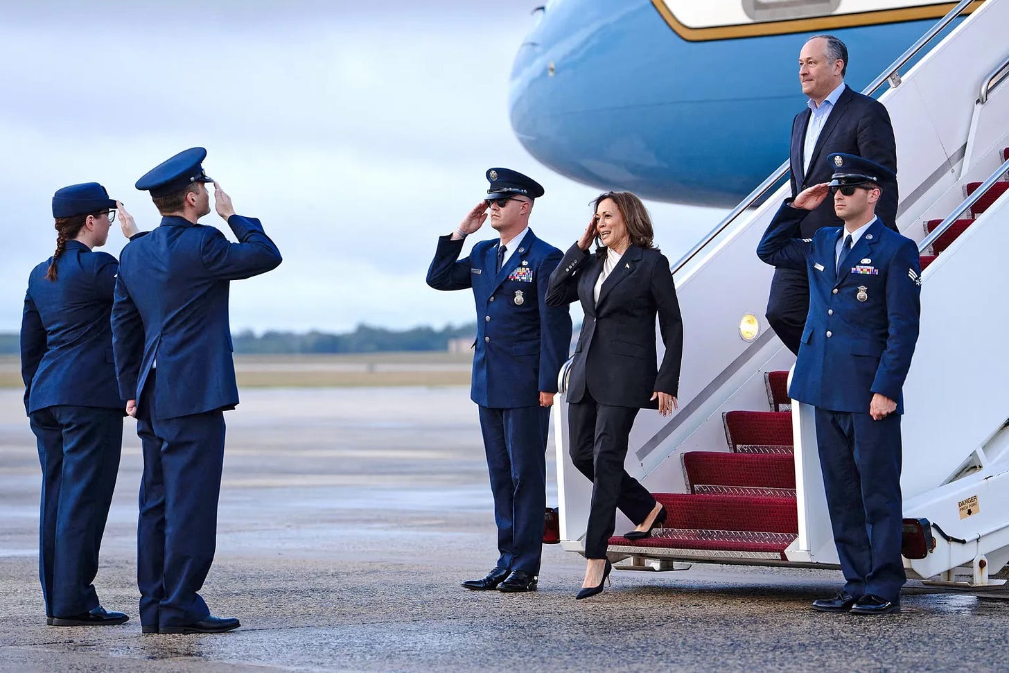 US Vice President Kamala Harris, with Second Gentleman Douglas Emhoff (R, top), salutes as she descends from Air Force Two at Delaware National Air Guard base in New Castle, Delaware, on July 22, 2024. Harris is set to meet campaign staff in Wilmington. Harris on Monday won the crucial backing of Democratic heavyweight Nancy Pelosi to lead the party against Donald Trump in November after Joe Biden's stunning exit from the 2024 race.  (Photo by Erin Schaff/Pool/AFP via Getty Images)