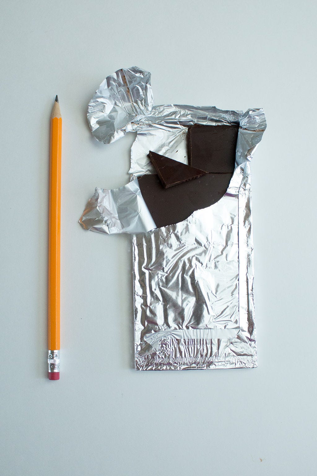 Dark chocolate broken into chunks in a silver wrapper next to a pencil