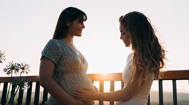 woman touching friend's pregnant belly with sunset in the background