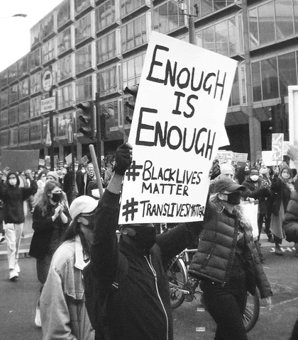 Gif con una scena tratta da una manifestazione: un uomo tiene tra le mani un cartello che dice "Enough is enough, #BlackLivesMatter, #TransLivesMatter"