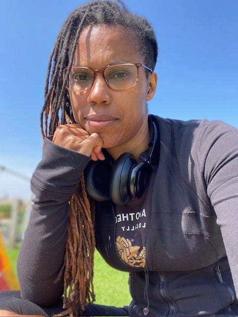 Sandra, a Black femme with locs, wearing glasses and a black jumper