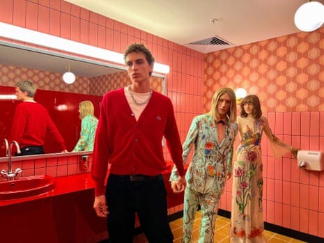 Man holding hands with one of two mannequins in a red-tiled public bathroom