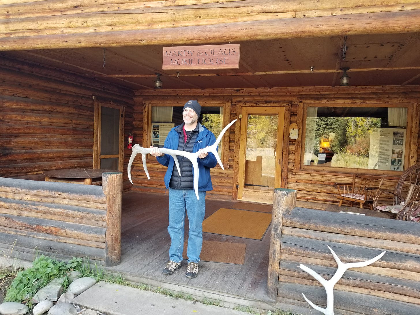 man on log cabin porch holding antlers