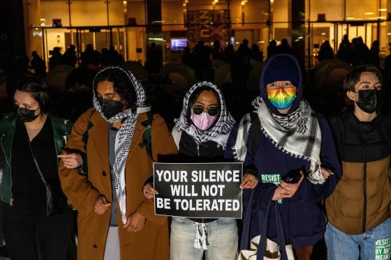 Photo of protestors wearing masks and keffiyehs with one holding a sign on New York University (NYU) campus.