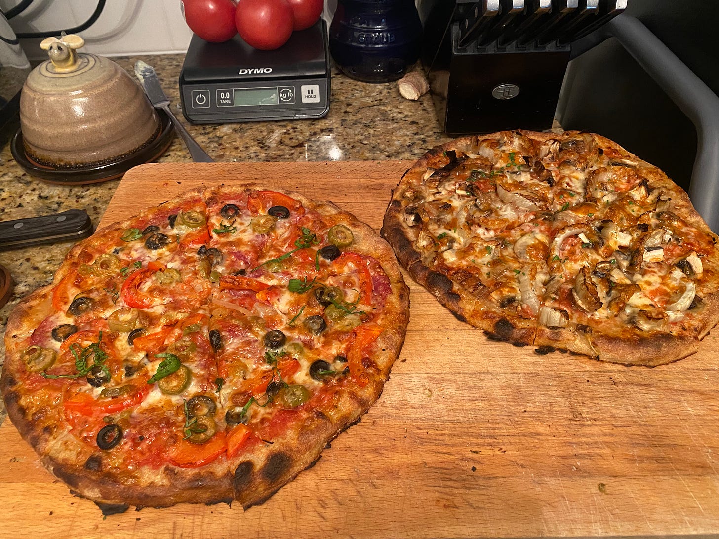 The two pizzas described above, on a wooden cutting board, the mushroom one on the right and the deluxe on the left.