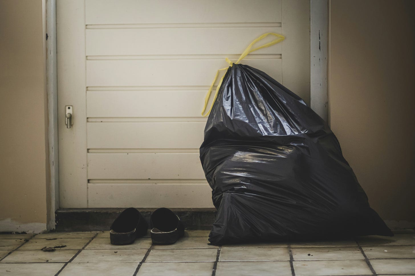 a single very full black garbage bag propped up against a white door