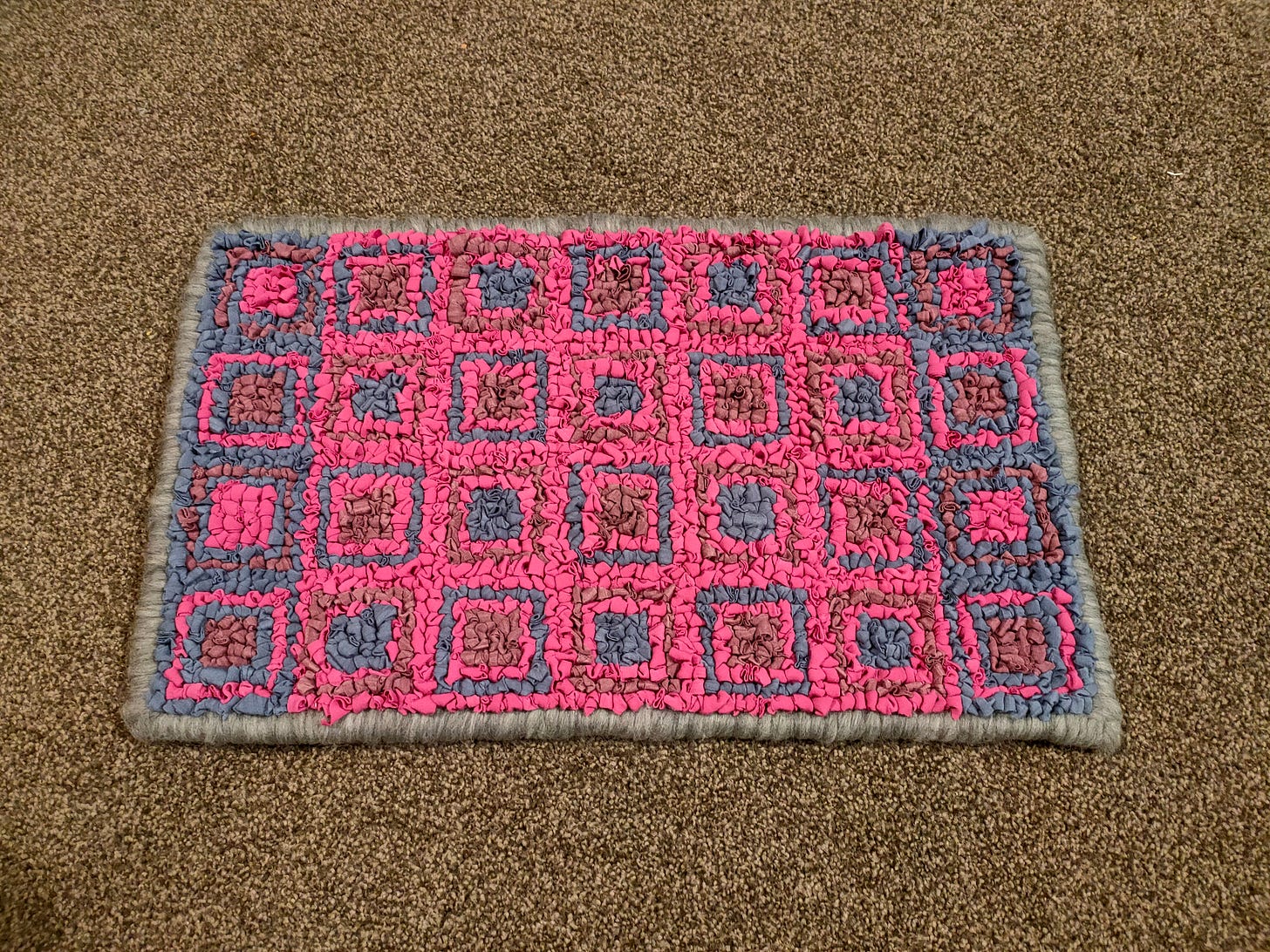 A loopy hooked rug made from blue, violet and pink merino strips, surrounded by a grey merino border. 