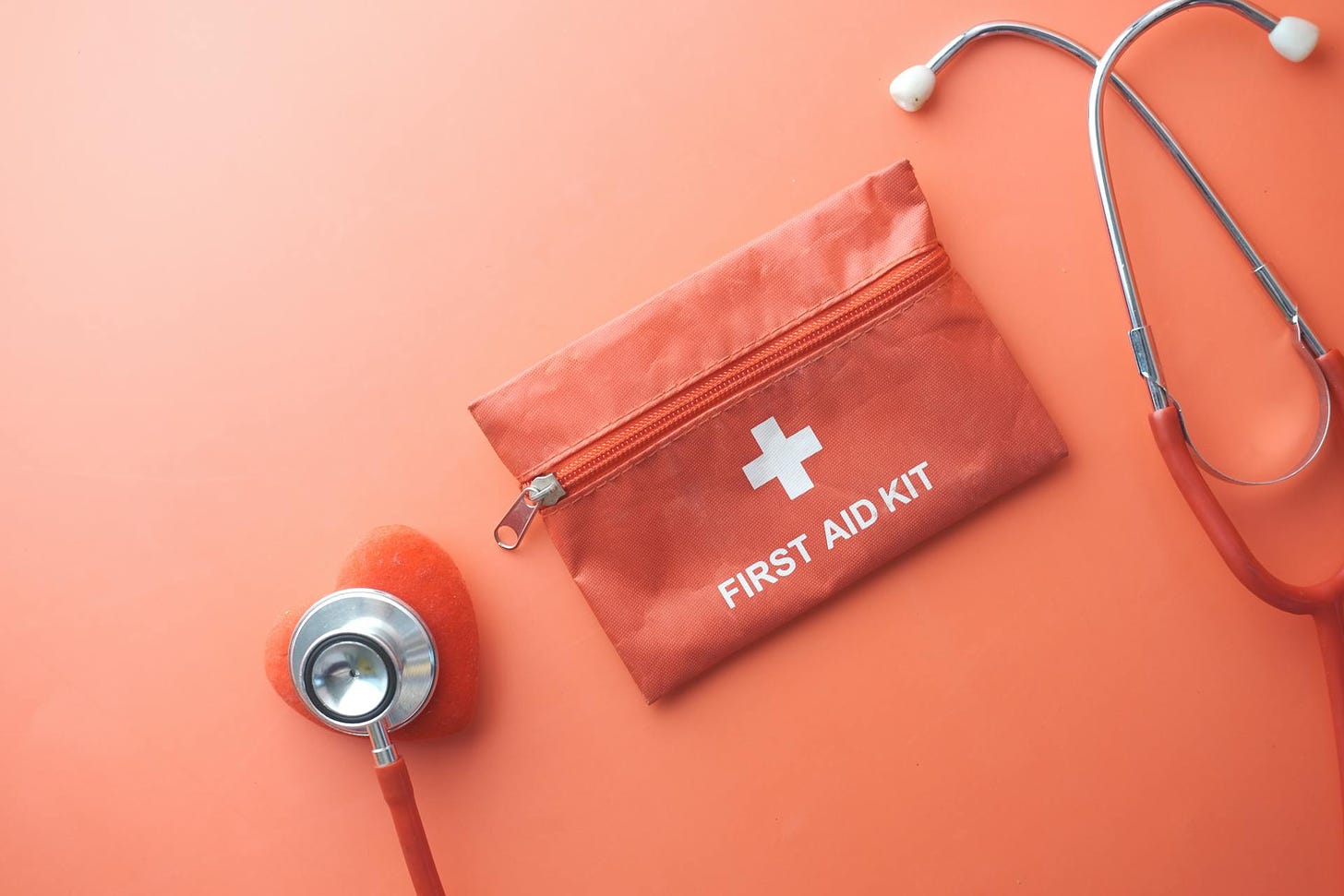 Photo of a First Aid kit and stethoscope with a heart shape at the end, against a red background