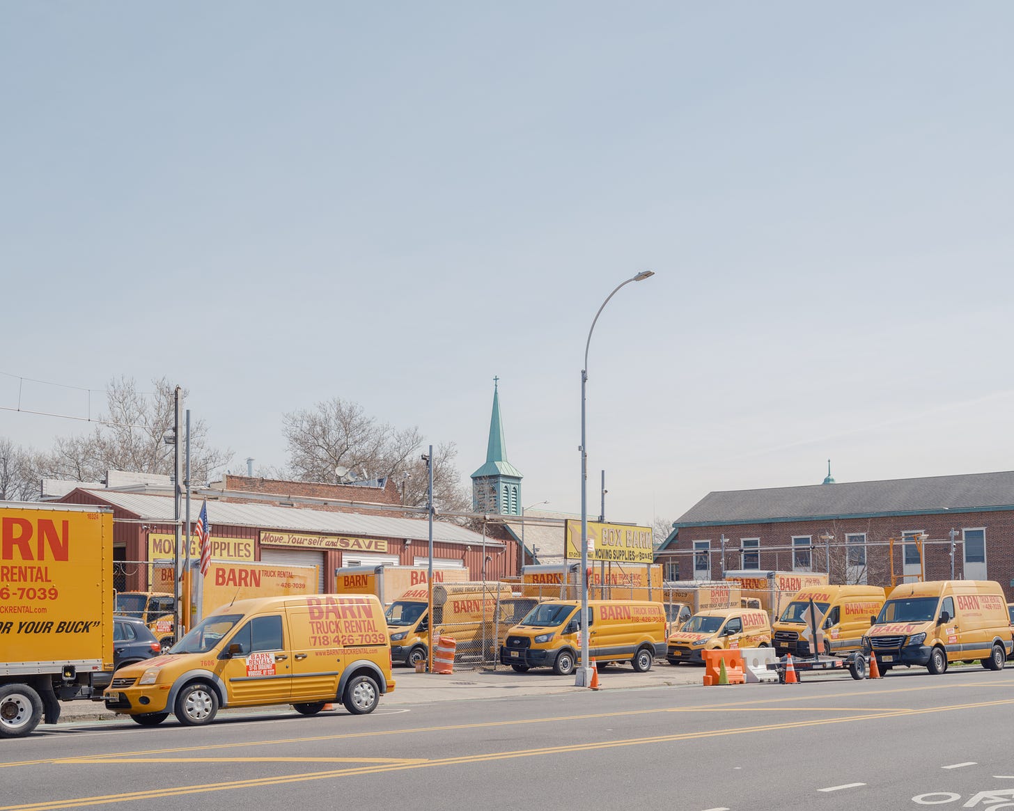 Fleet of yellow vans and trucks from Barn Truck rental with green church spire in the background