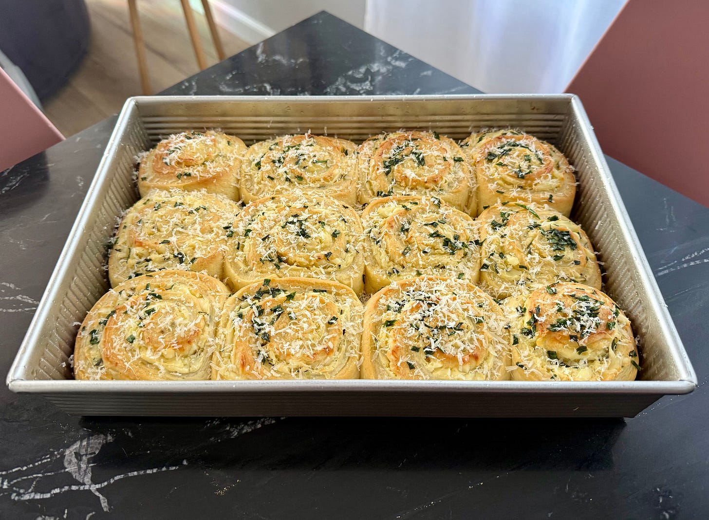 A pan of a dozen golden brown rolls topped with chives and parmesan