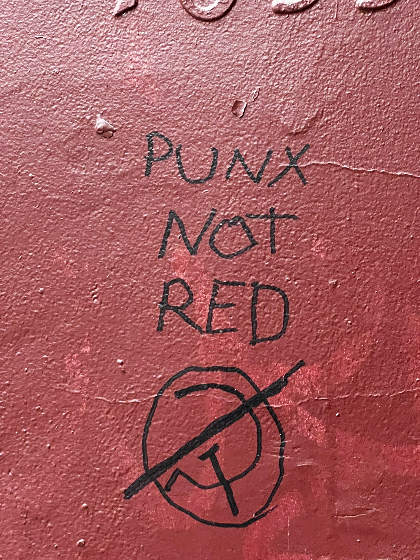 "punx not red" written in sharpie on a red wall with a hammer and sickle struck through below it