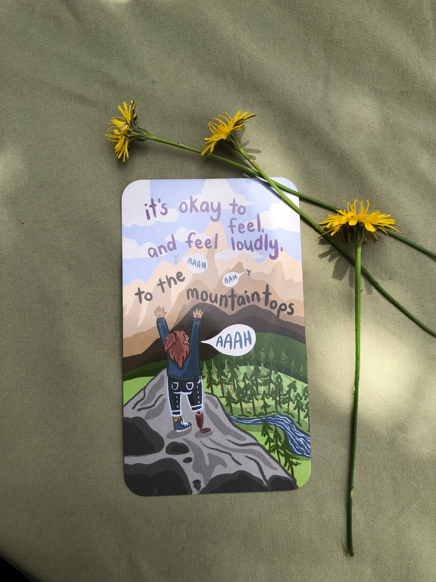 image of a Feely Card with an illustration of someone on a mountain, arms outstretched, with the quote "It's okay to feel loudly, to the mountaintops"