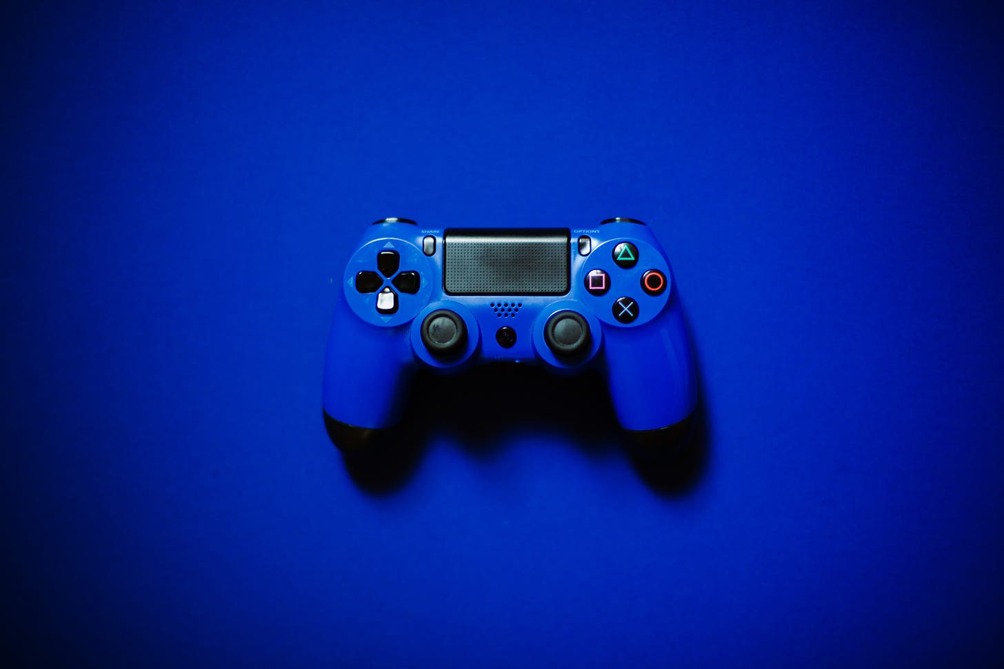 a blue playstation 4 controller against a darker blue background