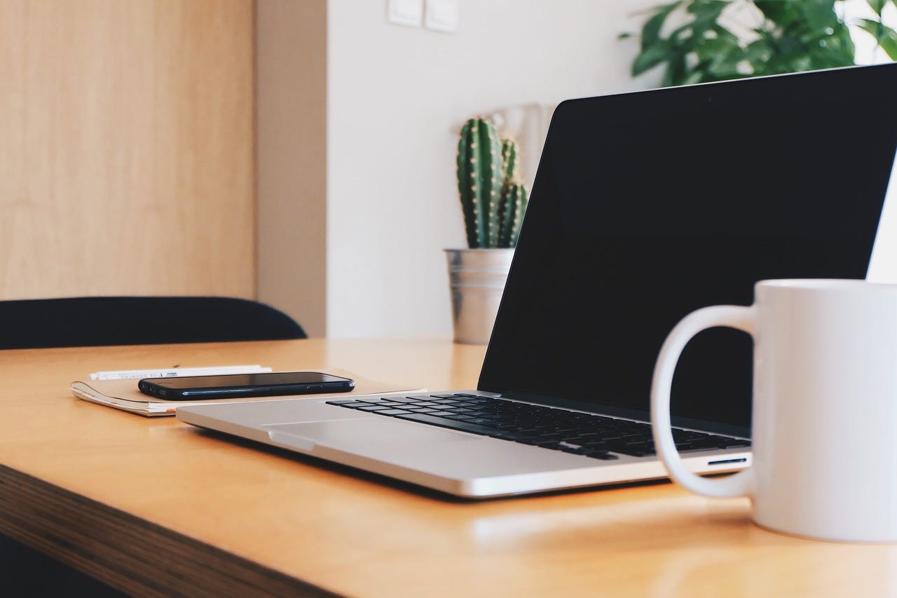 Desk with a laptop, notepad, phone, and coffee mug.