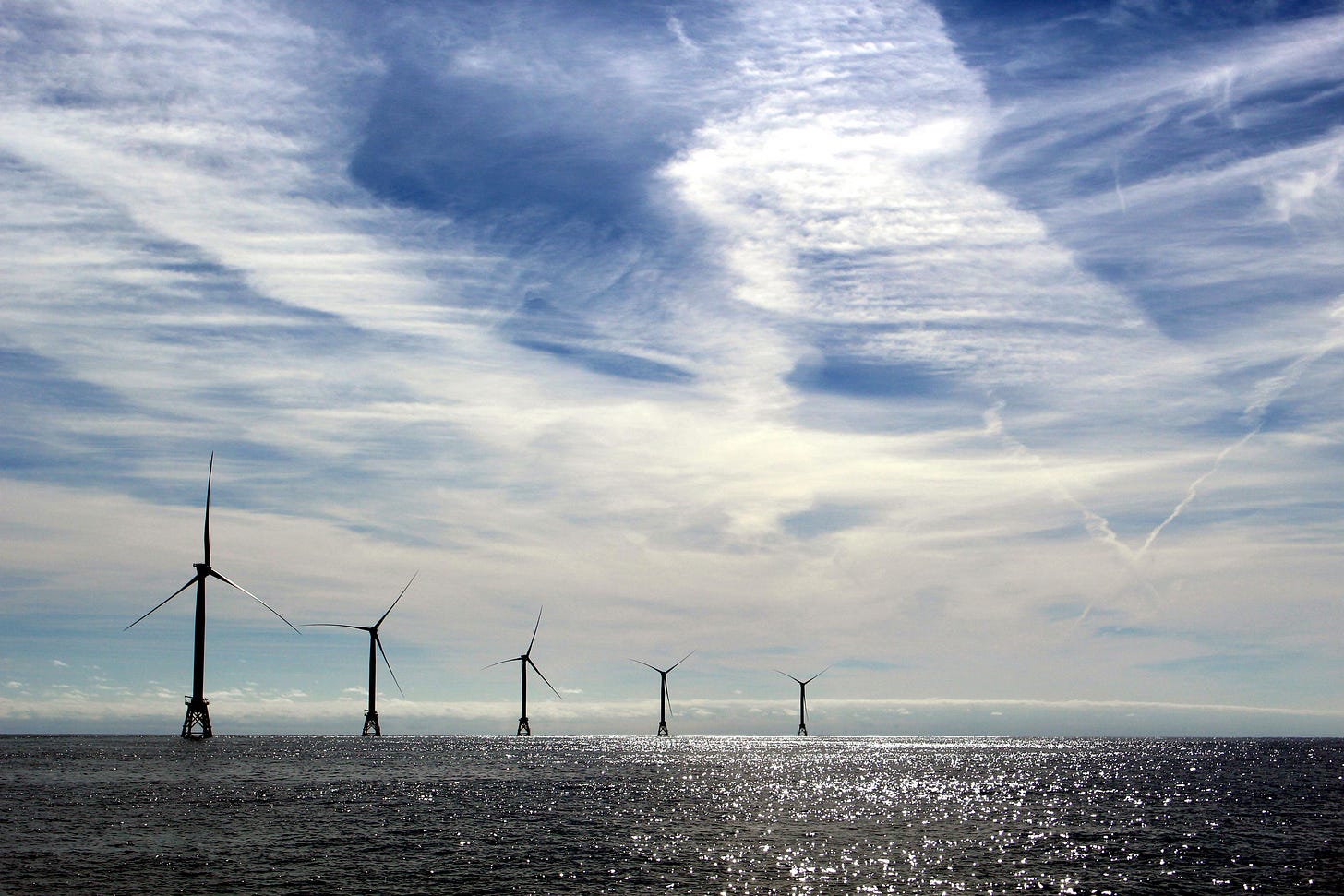 Five Block Island wind turbines recede into the distance on a semi cloudy day.