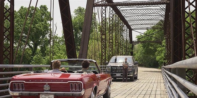 WAlker Micki blocking Cordell and Hoyt in red convertible on bridge.