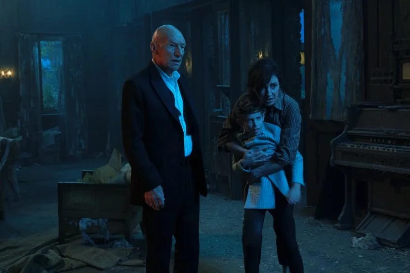 This image shows the tuxedo-clad Jean-Luc Picard (played by Patrick Stewart), Picard's princely younger self (who wears a crown and is played by Dylan Von Halle), and Tallinn (played by Orla Brady) standing in Château Picard's basement. Tallinn wraps her arm around Young Jean-Luc, while all three characters look aghast at something off screen. This image shows the tuxedo-clad Jean-Luc Picard (played by Patrick Stewart), Picard's princely younger self (who wears a crown and is played by Dylan Von Halle), and Tallinn (played by Orla Brady) standing in Château Picard's basement. Tallinn wraps her arm around Young Jean-Luc, while all three characters look aghast at something off screen.
