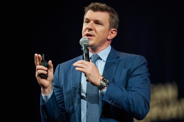 James O'Keefe wearing a suit and speaking into a microphone. 