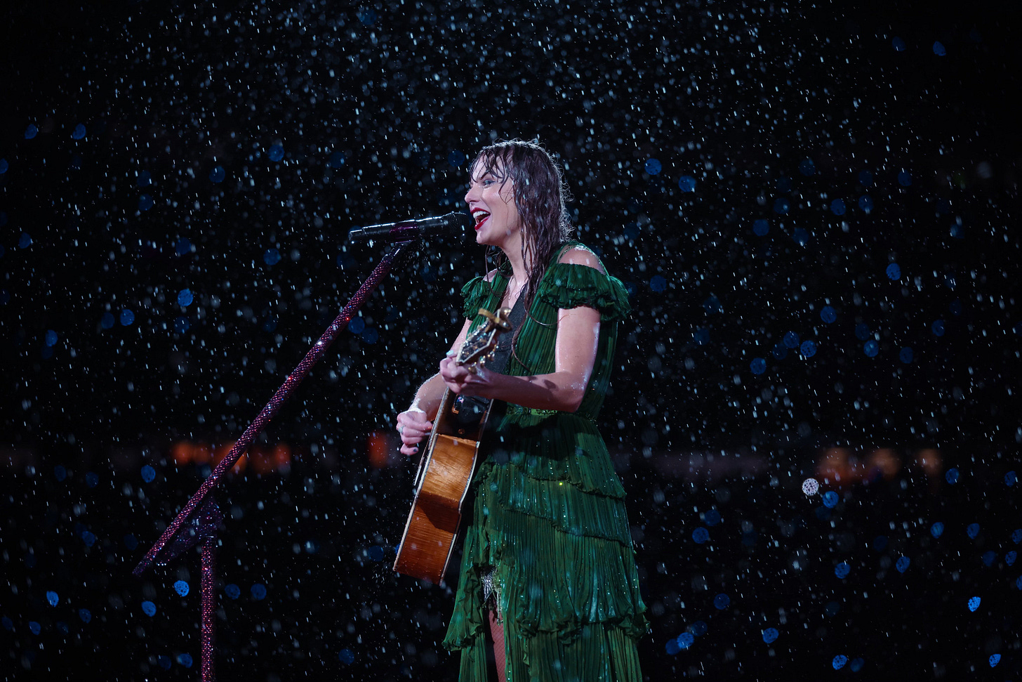 Taylor Swift singing in the rain while wearing a green dress and playing a guitar.