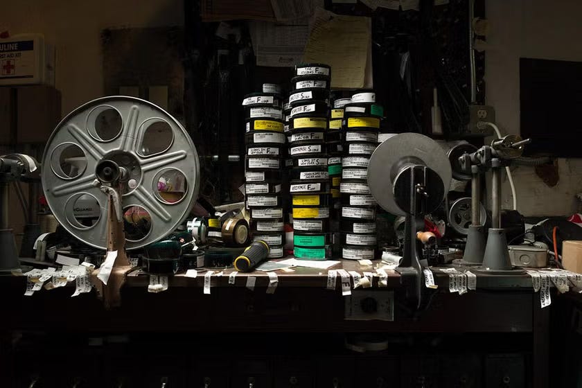 Photograph of a make-up table, where shipping reels of film are compiled onto a larger reel for screening. Dozens of rolls of 35mm film and handwritten labels are on the table.