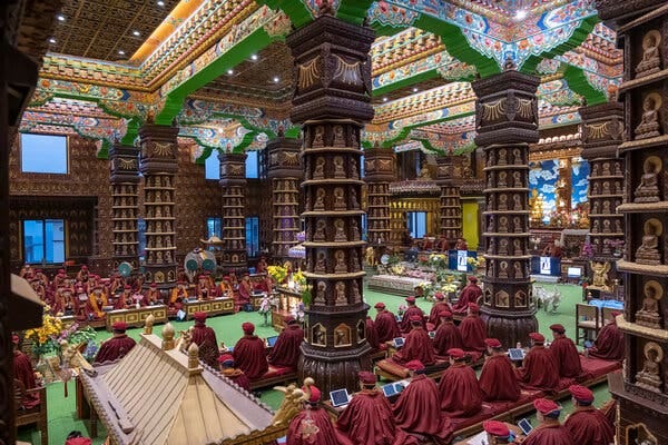A large group of nuns wearing maroon-colored robes in an ornately decorated, columned pray hall. 