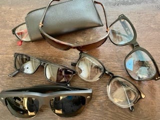 A collection of glasses. One is sticking out from a cheap case that came with them. Some look mad cheap because they were. Three are sunglasses.