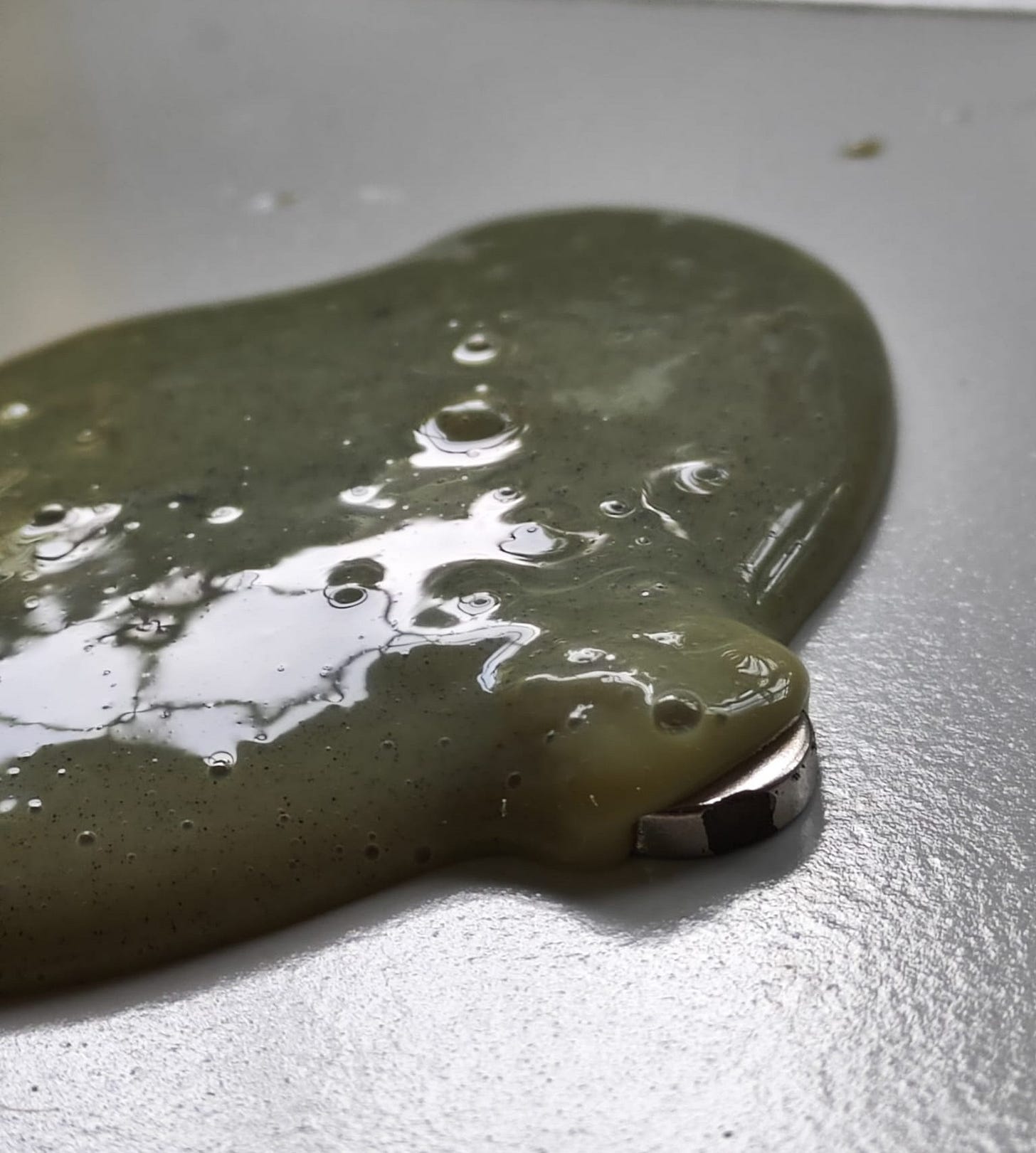 Mysterious, bubbling green goo overwhelms a magnet placed on a metal surface