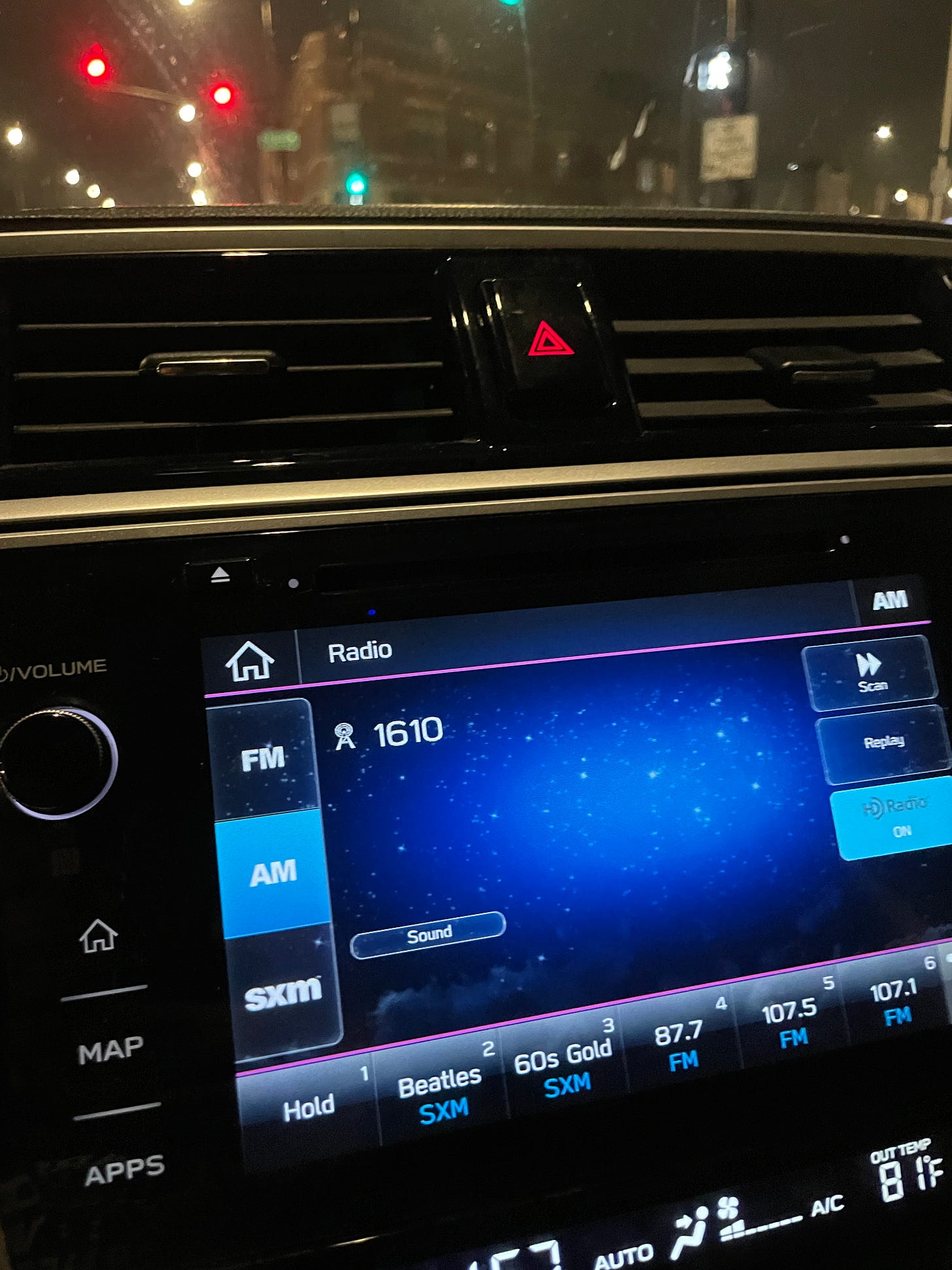 My car radio’s screen tuned to AM 1610, a Chicago street at night seen through the windshield.