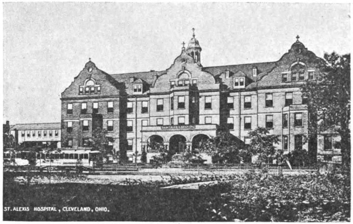 An ornate building with many windows and a doorway that features three arches. In front of the building there is a train. There are some trees on the right of the image.