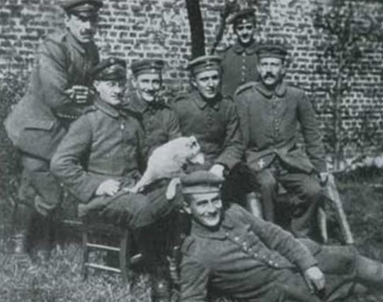 A black and white photo of a group of men in German army uniforms. There are a couple of excellent moustaches on display. On man has a dog on his lap. The dog has looked away from the camera at the critical moment.