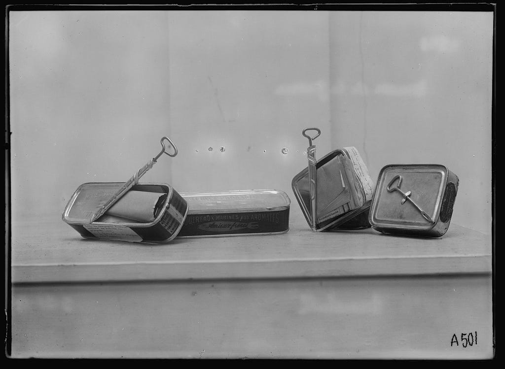 A black-and-white photograph of partially wound-open sardine tins, containing folded sheets of paper