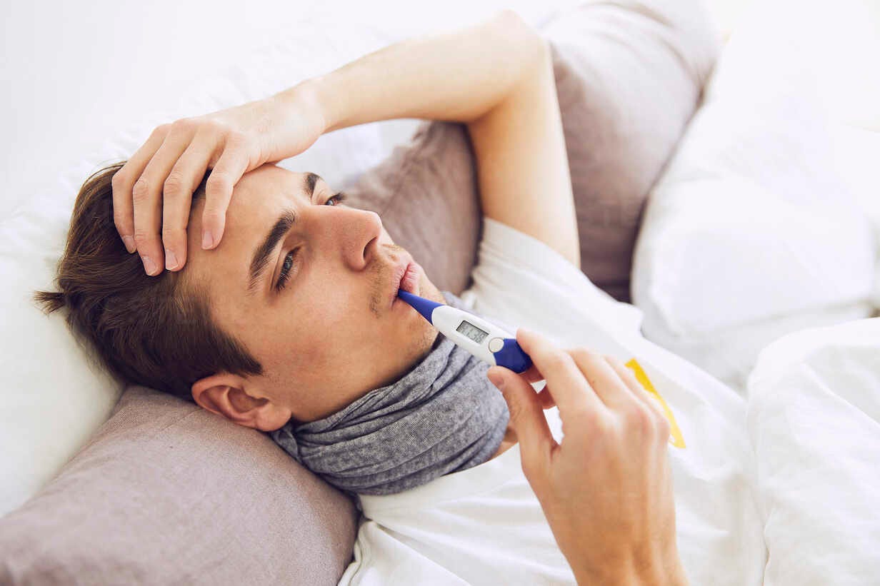 Close-up of sick man with thermometer in mouth resting on bed at home stock  photo