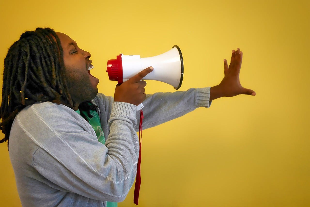 Black man with dreadlocks singing dramatically into a megaphone