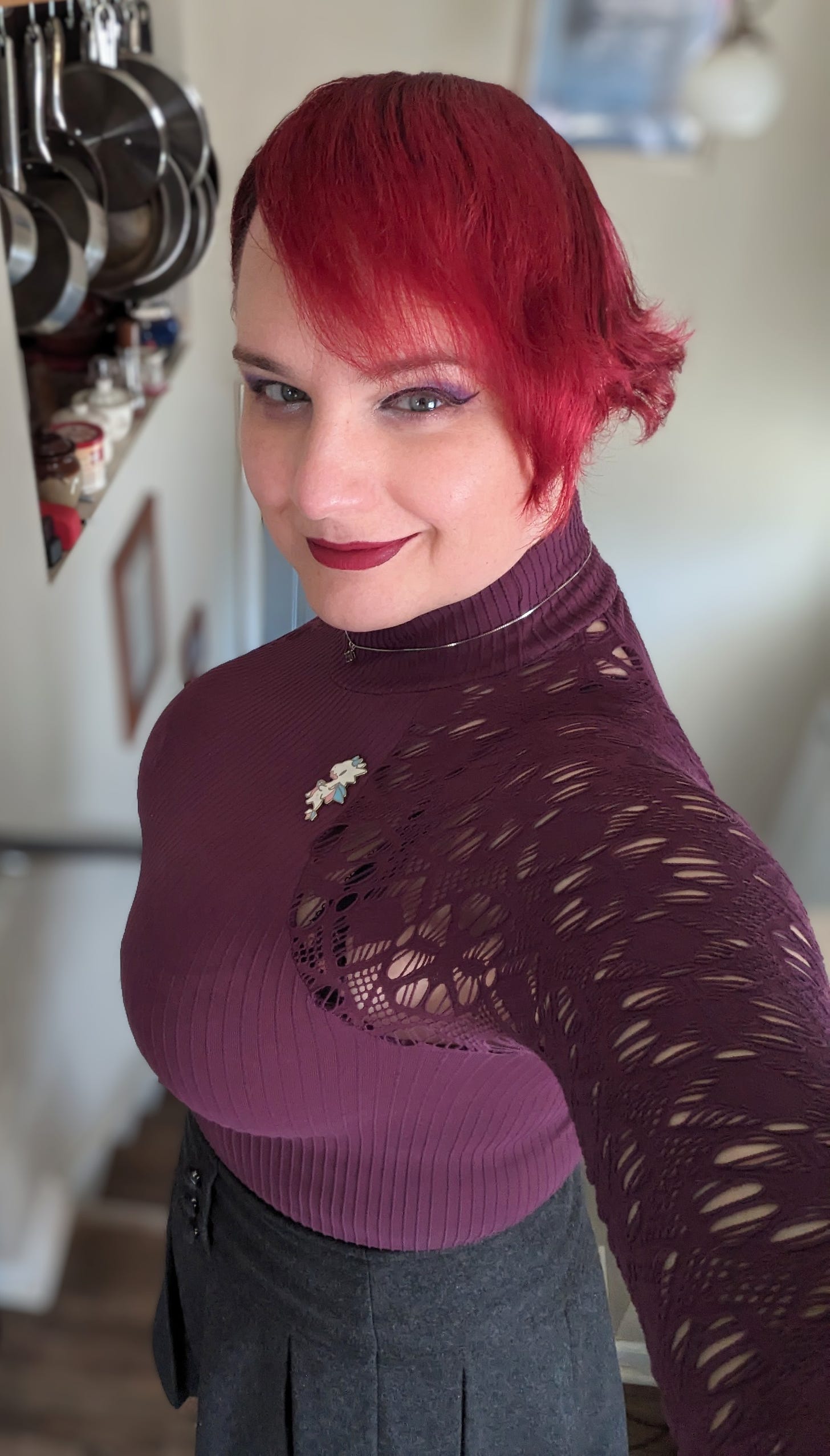 A redhead with a full head of hair, a clear face, and full bosom grins at the camera.