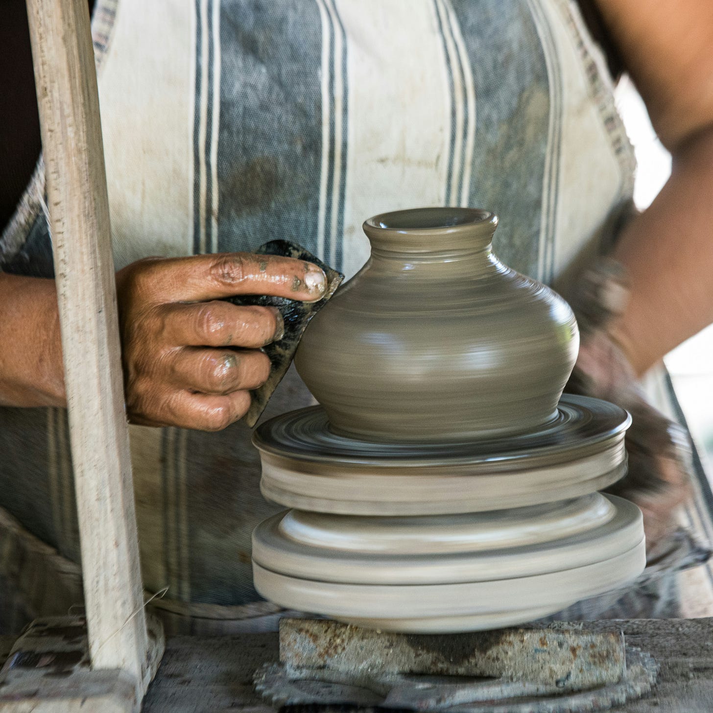 A pair of hands shaping a pot on a pottery wheel. 