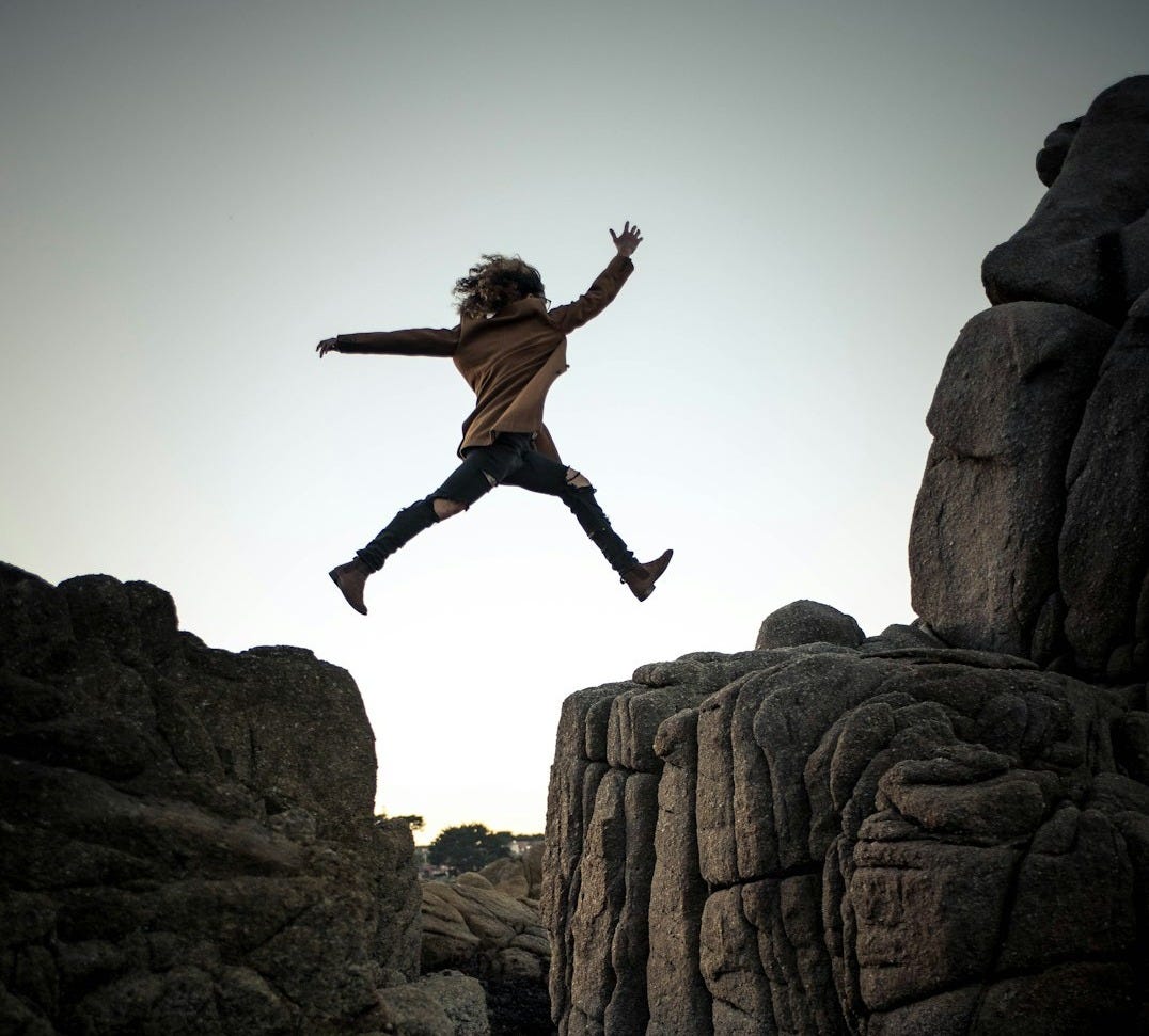 person jumping on big rock under gray and white sky during daytime person jumping on big rock under gray and white sky during daytime
