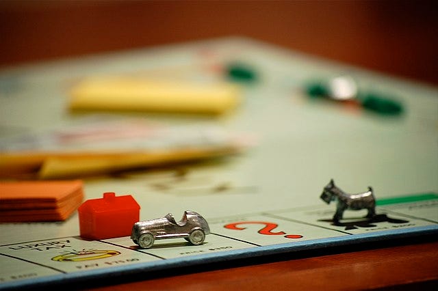 Photograph of monopoly board, with car and dog pieces in focus. the dog is chasing the car