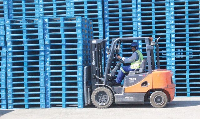 Forklift moving blue Chep pallets in an outdoor storage area