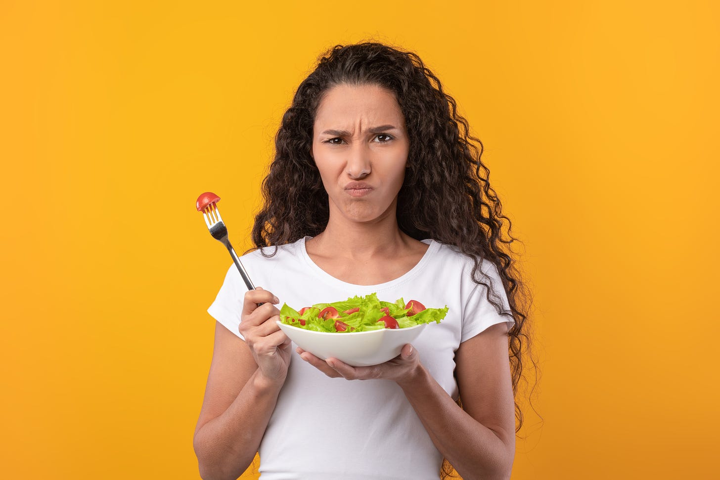 Woman holding a bowl of vegetables, looking skeptical