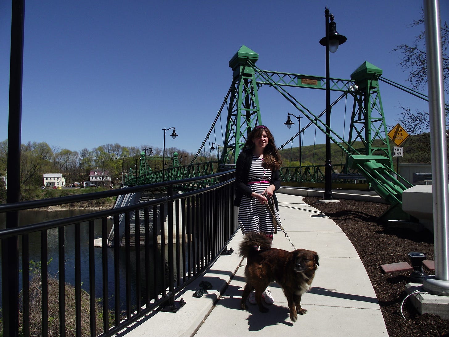 Photo of the author with her dog in front of an old metal river bridge.