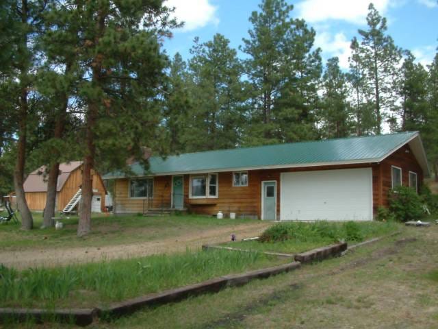 left to right, a barn, pine trees, and a small, simple house, wood with a green roof and green doors