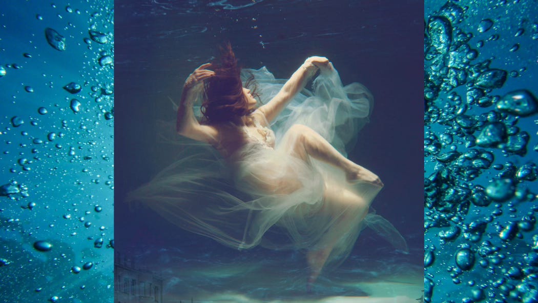 A woman in a diaphanous white dress lies suspended in deep water.